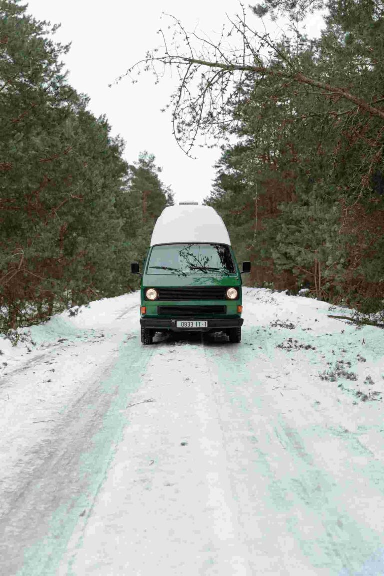A campervan travels on a snowy forest road, showcasing a serene winter landscape ideal for adventure travel.